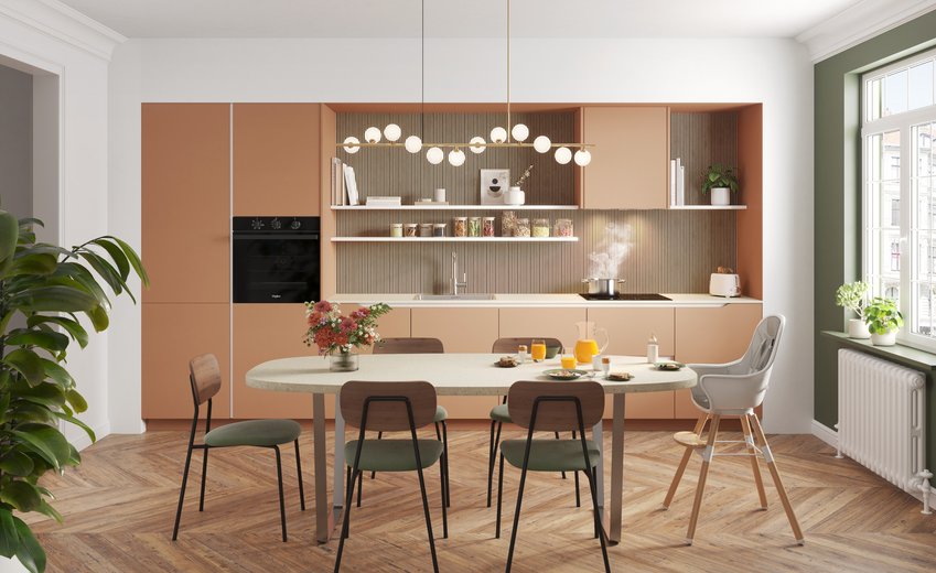 Moderne keuken in koraalkleur, spatwand met houten lattenstructuur, open schappen, en grote ovale tafel met grijsgroene stoelen.